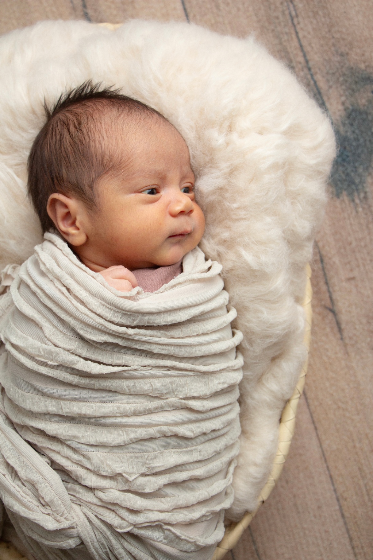 Newborn wrapped in cream resting in a woven basket